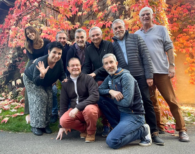 Groupe de dix personnes posant ensemble devant un mur recouvert de feuilles d'automne colorées.